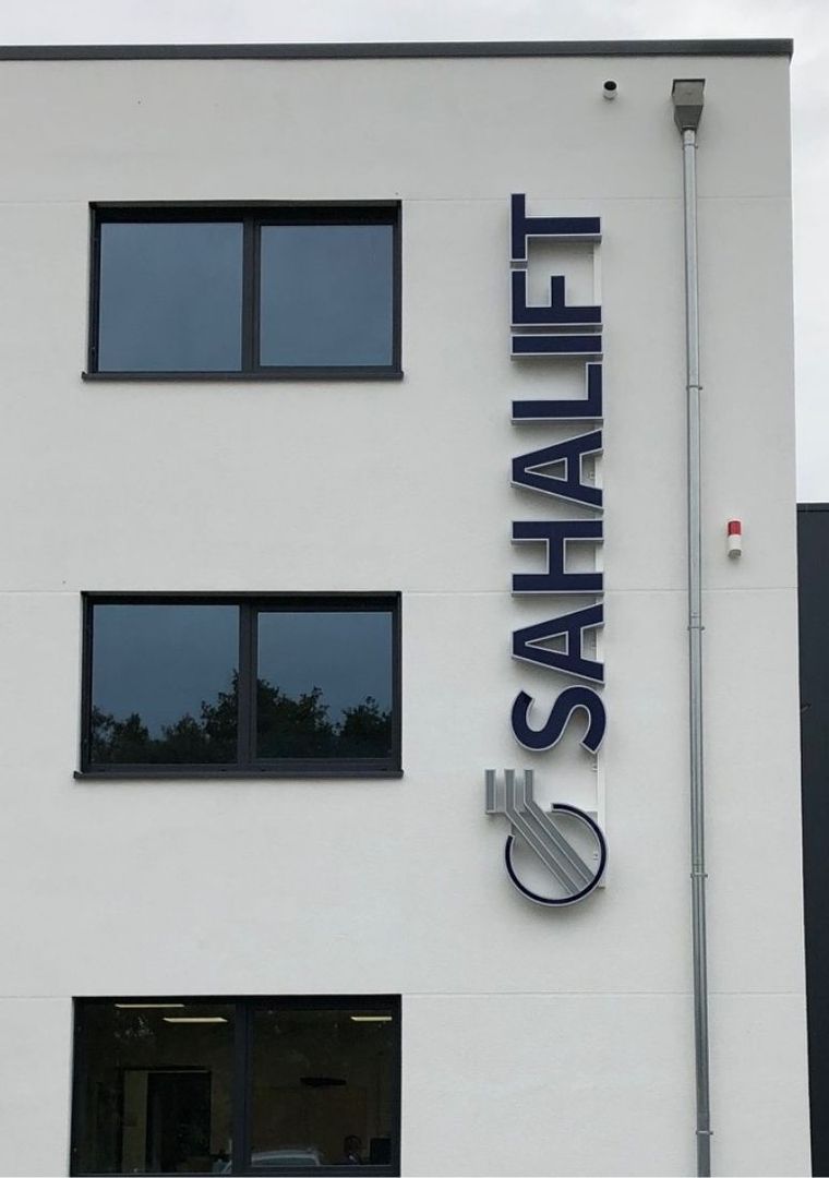 Außenansicht eines modernen Gebäudes mit großen Fenstern und einem blauen Schild mit der Aufschrift "SAHALIFT".